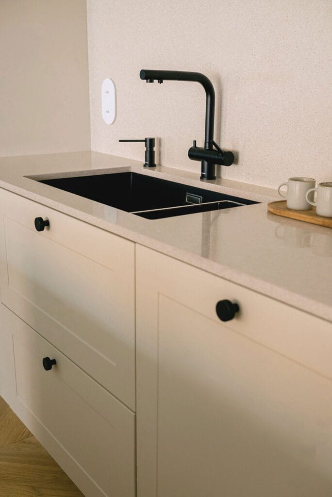 Czarne baterie kuchenne na tle jasnego blatu i beżowych szafek w nowoczesnym wnętrzu.