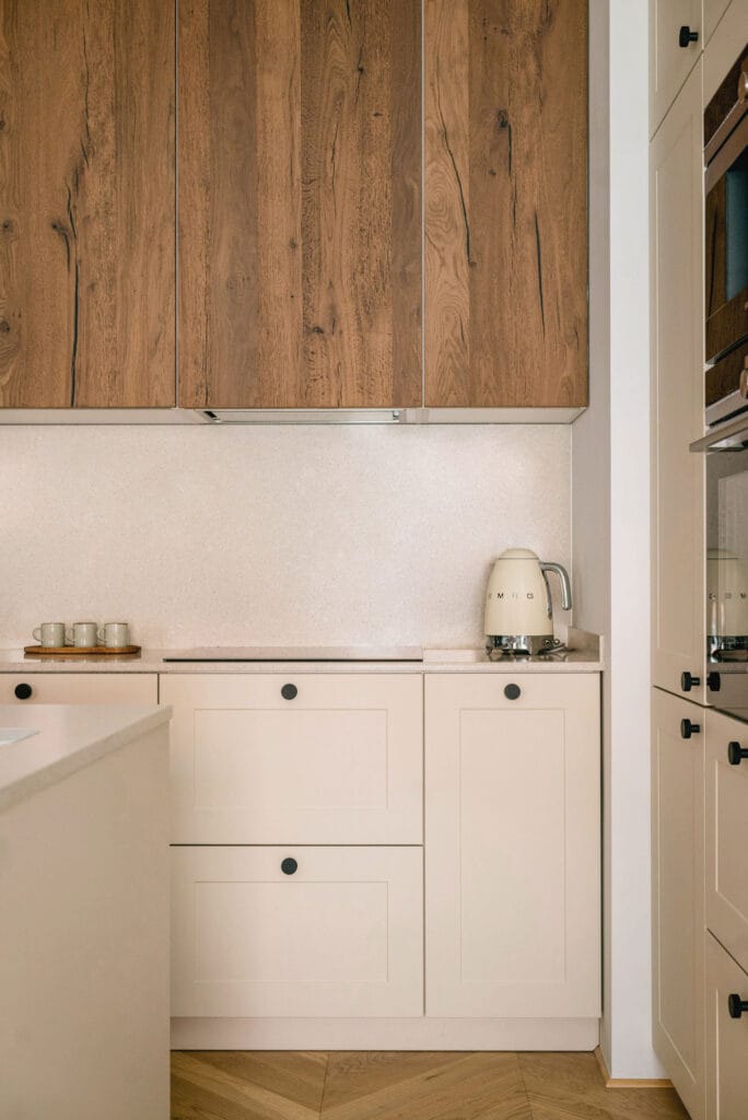 Minimalistyczna kuchnia z drewnianymi szafkami i beżowymi frontami, wyposażona w stylowy czajnik i zestaw filiżanek na blacie.