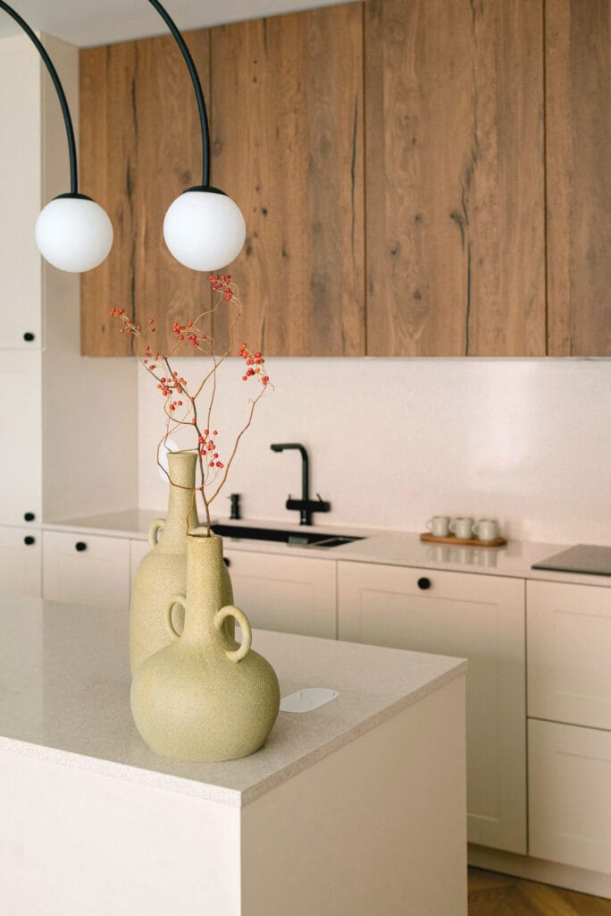 Nowoczesna kuchnia z wyspą, drewnianymi akcentami i stylowym oświetleniem, zachowana w ciepłych barwach.