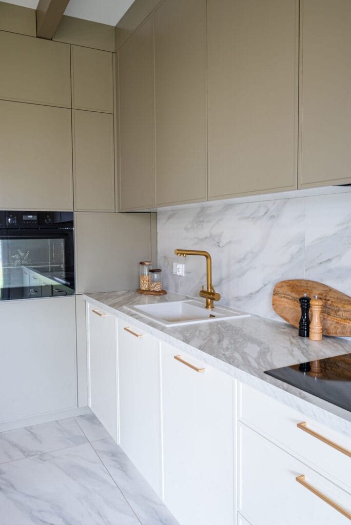 Kuchnia w minimalistycznym stylu z beżowymi szafkami, złotymi detalami i nowoczesnym piekarnikiem do zabudowy.