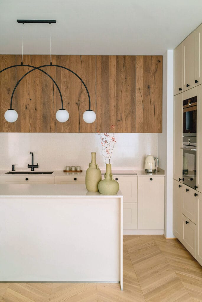 Nowoczesna kuchnia z drewnianymi frontami, jasnym blatem i czarną baterią kuchenną, uzupełniona eleganckimi detalami.