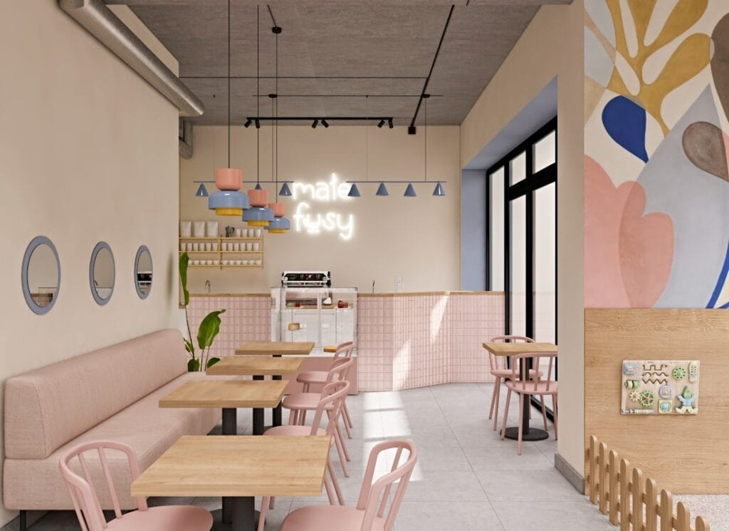 Wnętrze kawiarni w pastelowych kolorach, z różowymi krzesłami, drewnianymi stolikami i neonowym napisem „małe fusy” na ścianie.